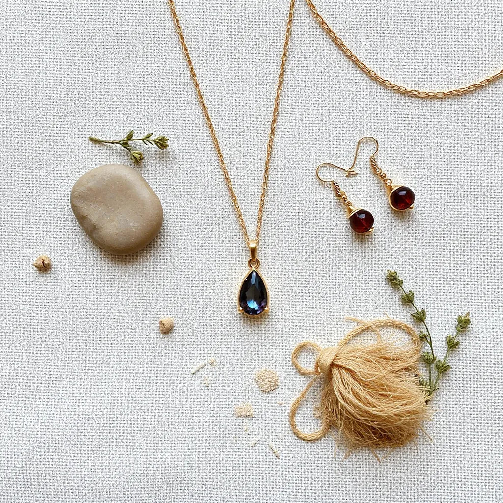 Necklace, earrings, and bracelet with gemstone charms arranged on neutral fabric with natural stones