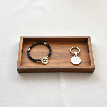 Minimal tray with personalized bracelet, engraved pendant necklace, and custom keychain under soft natural light.